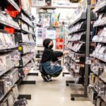 A konbini culture worker restocking fresh food shelves inside a brightly lit Tokyo convenience store at night
