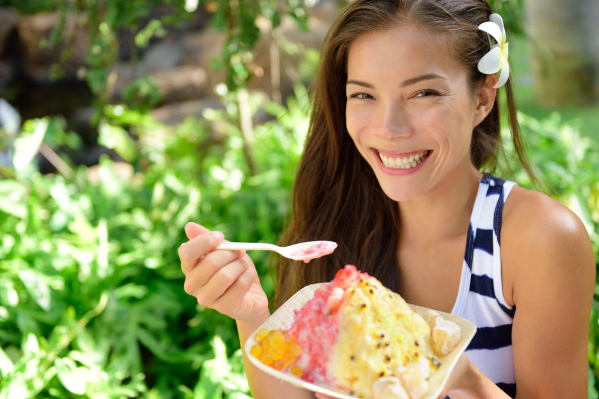 A woman savors a bowl of kakigori at aTokyo shop, holding a small spoon over a mountain of shaved ice with fresh fruit syrup.