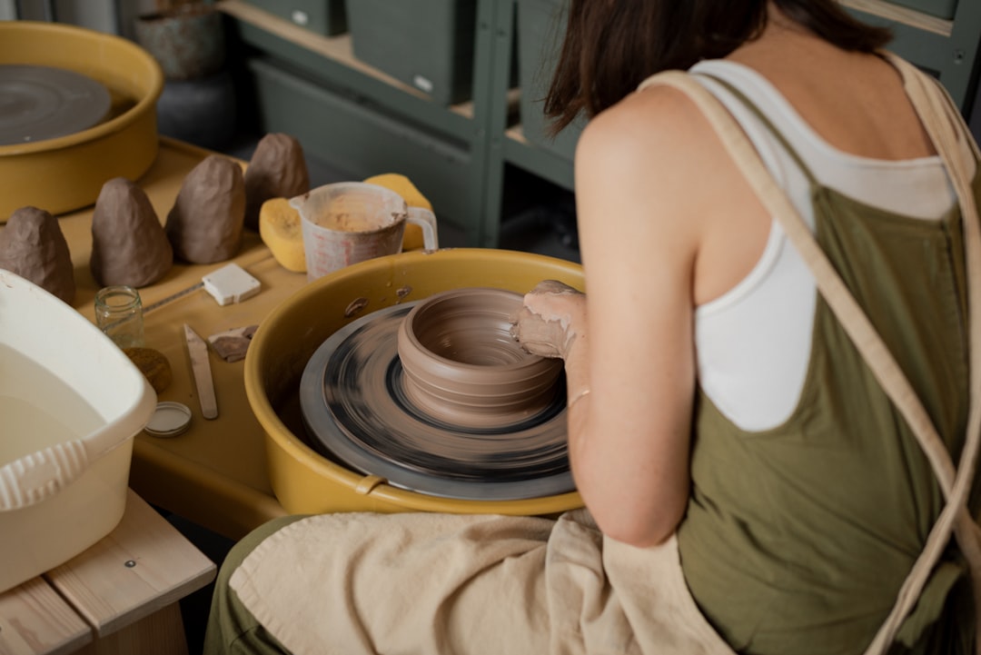 A woman shaping clay at a Tokyo workshop pottery wheel, focused and covered in clay dust