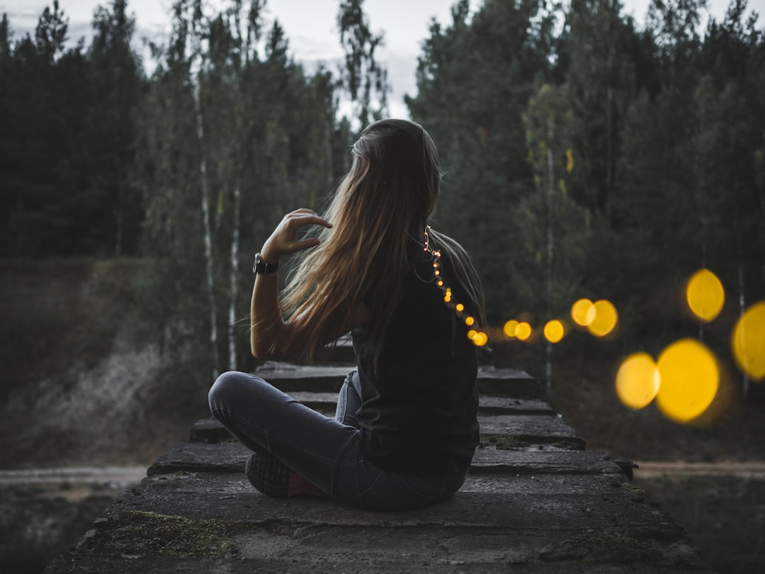 A woman stands quietly beside the River during a Fussa firefly viewing evening, watching soft lights reflect on the water