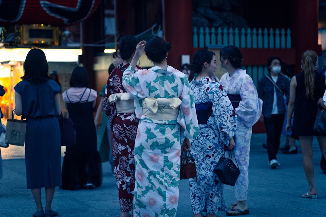 A woman in a yukata smiles while watching the Hanabi Tokyo fireworks show at night, surrounded by a crowd of festival-goers.