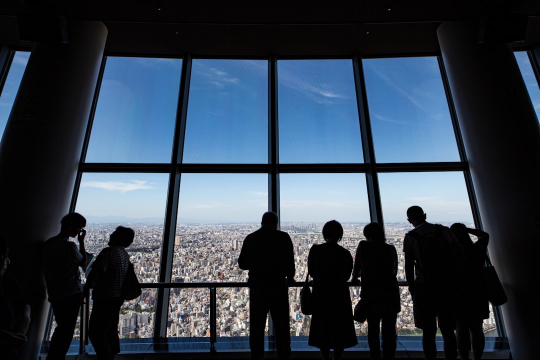 A business executive reviews documents at a Tokyo headquarters office, with a city skyline visible through the window.
