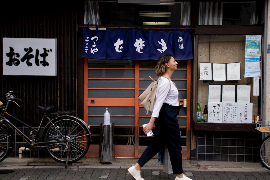 A woman dressed in loose natural Japanese fabrics walks through a shaded Tokyo street on a hot August afternoon